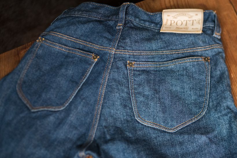 Rückansicht einer blauen Jeans mit zwei aufgesetzten Taschen und dem Lederlabel von POTT am Bund.