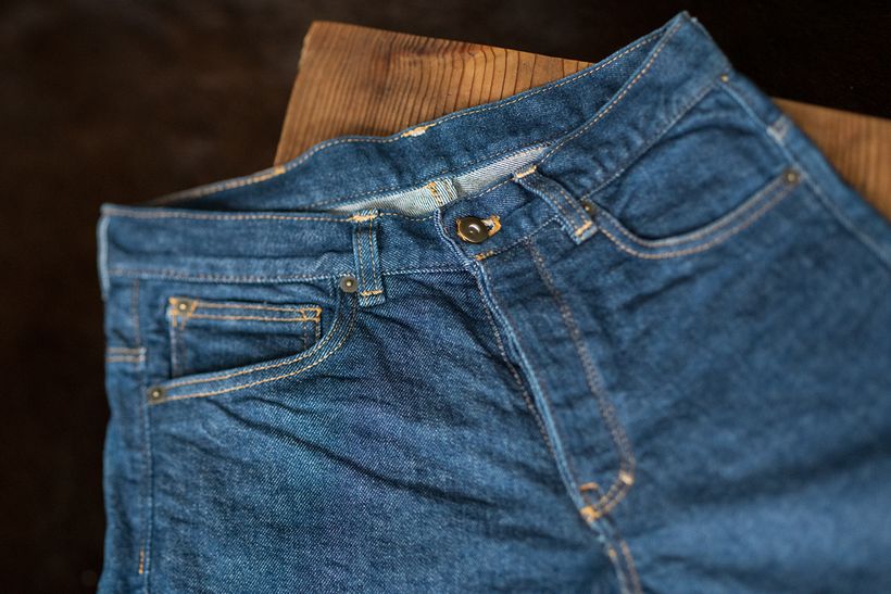 Zusammengelegte blaue Jeans auf einer Holzfläche, Blick auf Bund, Knopfleiste und Vordertaschen.