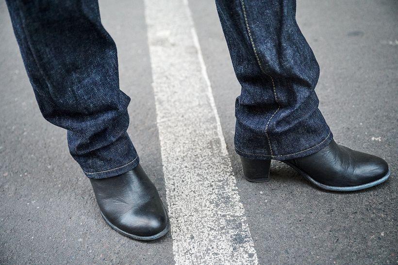 Zwei Hosenbeine aus dunklem Denim über schwarzen Stiefeletten auf Asphalt.