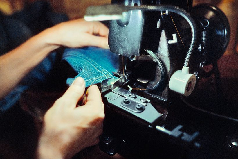 Hände führen ein Jeansbein durch die Union-Special-Kettenstichmaschine.