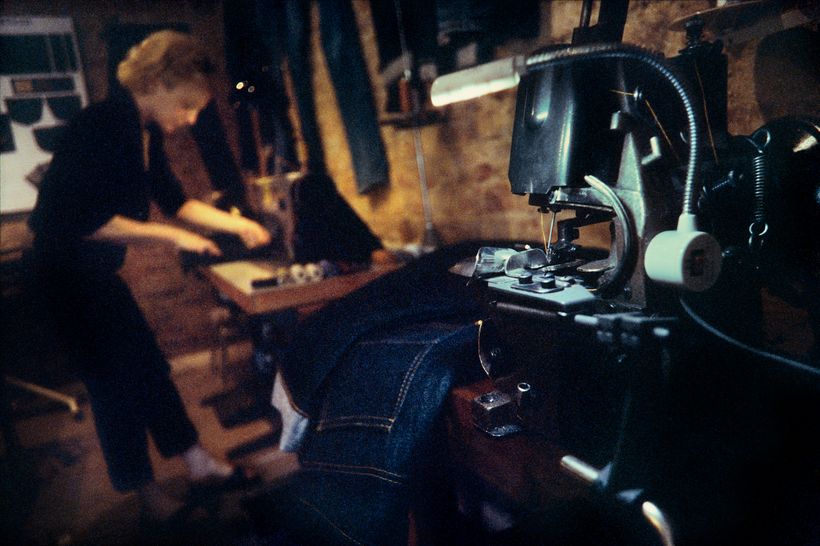 Blick in die Werkstatt: Manuela Pott arbeitet am Zuschneidetisch, im Vordergrund eine Nähmaschine mit eingelegter Jeans.