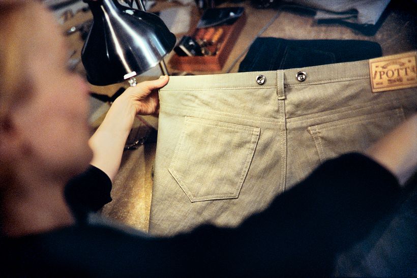 Eine helle Hose wird unter der Werkstattlampe geprüft, am Bund das Lederlabel von POTT.