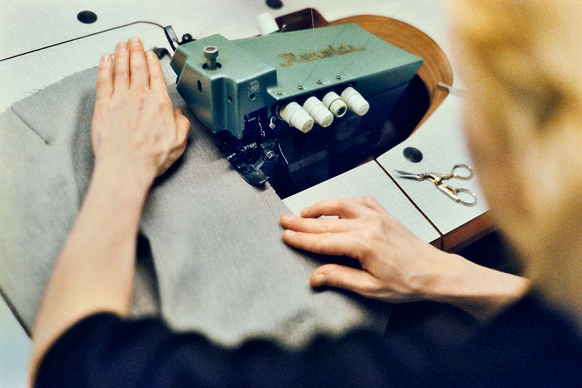 Zwei Hände führen hellen Wollstoff über eine alte grüne Nähmaschine.