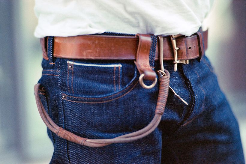 Nahaufnahme der Hüftpartie: eine dunkle Jeans mit braunem Ledergürtel, an der Gürtelschlaufe hängt ein Schlüsselband.