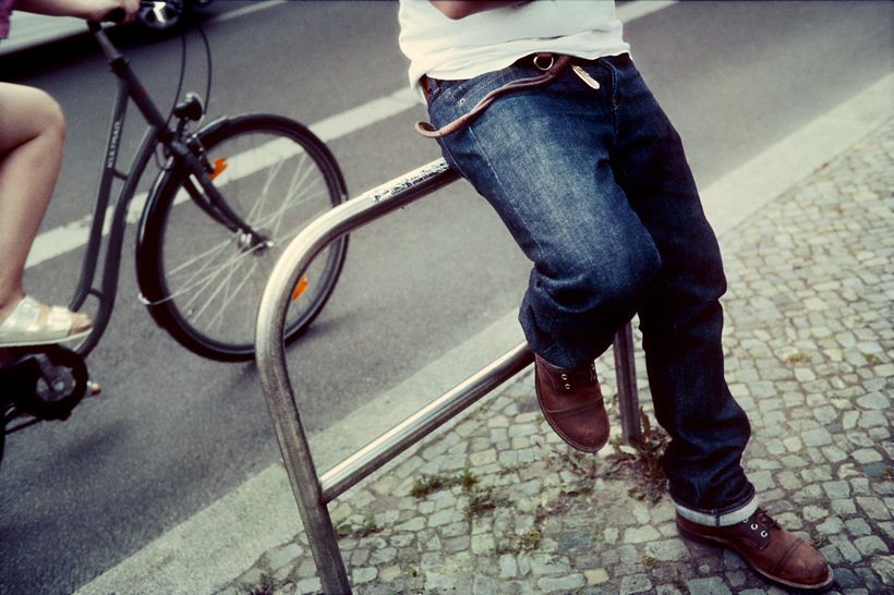 Eine Person in einer Jeans von POTT lehnt an einem Fahrradständer.